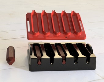 Op de afbeelding: Een rode plastic bak met zes gleuven om hotdogs in te bewaren, en een zwarte plastic bak met zes gleuven om hotdogs in te bewaren.