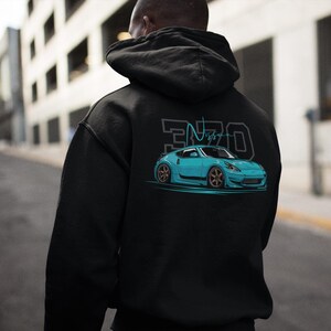 May include: Black hooded sweatshirt featuring a teal sports car graphic with the text "370 Nismo". The car has bronze-colored rims and is set against a teal background. The sweatshirt is a casual streetwear item.