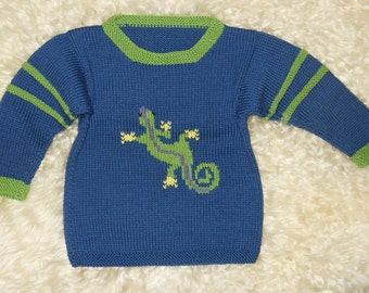 Könnte beinhalten: Ein blauer Strickpullover mit grünen Streifen an den Ärmeln und einem grünen Eidechsen-Design auf der Vorderseite.
