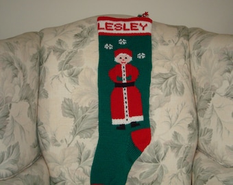 Könnte beinhalten: Ein grüner, gestrickter Weihnachtsstrumpf mit einem roten und weißen Weihnachtsmann-Motiv. Der Strumpf trägt den Namen "LESLEY" gestickt.