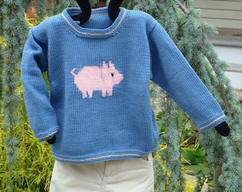Könnte beinhalten: Ein blauer Strickpullover mit einem rosa Schweinemotiv. Der Pullover hat einen weißen Saum an Hals und Ärmeln. Der Pullover hängt an einem Kleiderbügel.