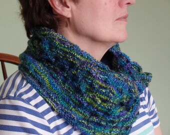 Könnte beinhalten: Eine Frau trägt einen blauen, grünen und violetten gestrickten Schal mit Rollkragen. Der Schal ist aus weichem, strukturiertem Garn gefertigt und hat ein einzigartiges, abstraktes Muster.