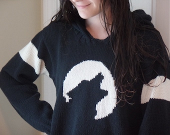 Könnte beinhalten: Ein schwarz-weiß gestreifter Kapuzenpullover mit einem weißen Halbmond- und Stern-Design.