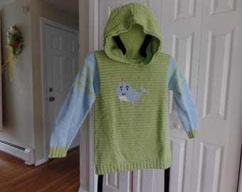 Könnte beinhalten: Ein grüner und blauer Kapuzenpullover mit einem Narwal-Motiv. Der Pullover hat an den Ärmeln ein hellblaues und grünes Streifenmuster.