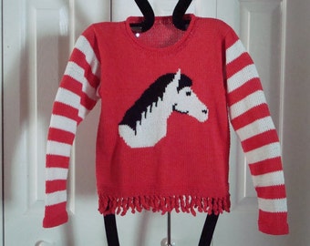 May include: Red knitted sweater with white and red striped sleeves and a white horse head design. The sweater has a fringe trim at the bottom.