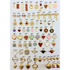 K&ouml;nnte beinhalten: Eine Sammlung goldfarbener Charms mit verschiedenen Designs, darunter Herzen, Schleifen und Anh&auml;nger mit dem Wort "LOVE" und dem Satz "I'M GOOD". Einige Charms weisen farbige Emaille-Akzente in Rot, Rosa und Blau auf.