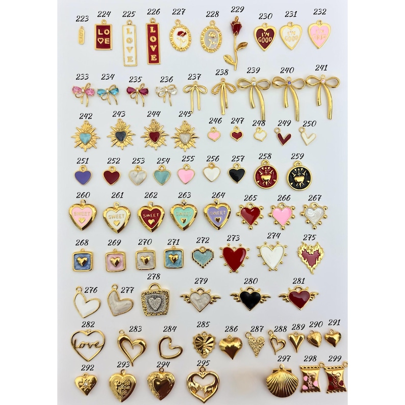 K&ouml;nnte beinhalten: Eine Sammlung goldfarbener Charms mit verschiedenen Designs, darunter Herzen, Schleifen und Anh&auml;nger mit dem Wort "LOVE" und dem Satz "I'M GOOD". Einige Charms weisen farbige Emaille-Akzente in Rot, Rosa und Blau auf.