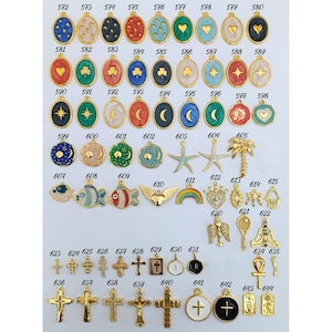 K&ouml;nnte beinhalten: Eine Sammlung goldfarbener Anh&auml;nger mit verschiedenen Designs, darunter Herzen, Kleebl&auml;tter, Sterne, Kreuze und Himmelsmotive. Die Anh&auml;nger sind oval, rund und in anderen Formen gehalten, mit farbigen Emaille-Akzenten.