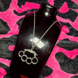 Op de afbeelding: Een zilveren ketting met een grote, zilveren, met strass bezette, knokkelstoot-hanger.