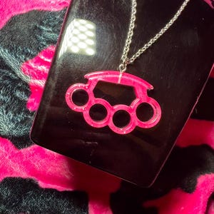 May include: A pink glitter knuckle duster pendant on a silver chain necklace.