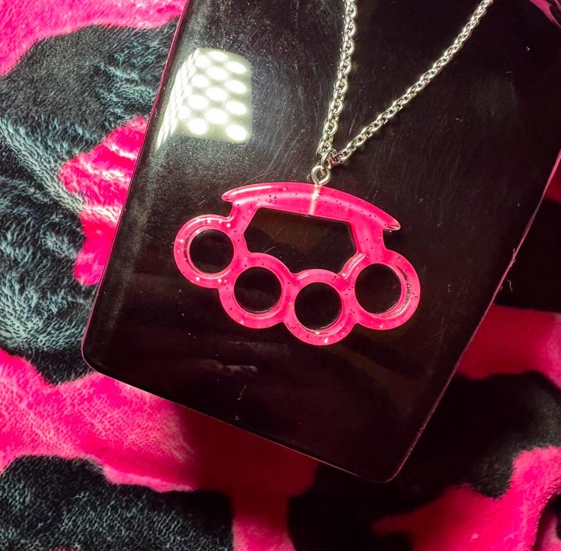 May include: A pink glitter knuckle duster pendant on a silver chain necklace.
