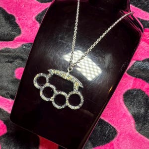 May include: A silver chain necklace with a sparkly silver-toned brass knuckle pendant.