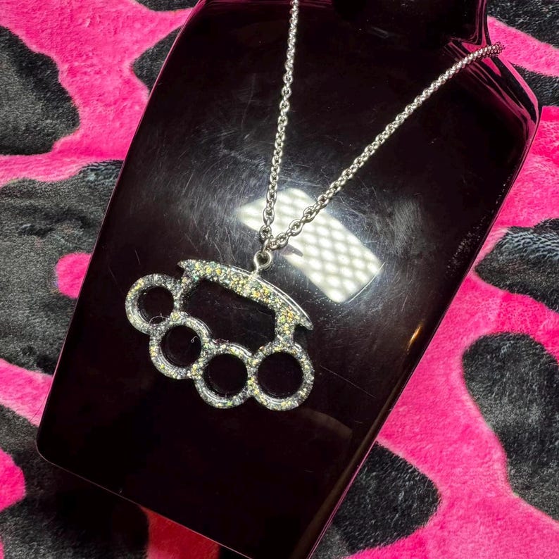 May include: A silver chain necklace with a sparkly silver-toned brass knuckle pendant.