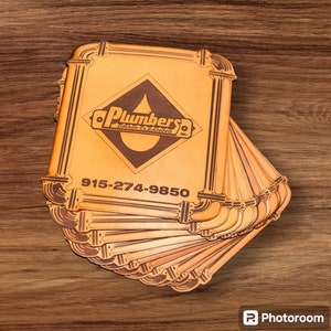 Könnte beinhalten: Ein Stapel brauner Lederuntersetzer mit einem Logo, das "Plumbers Drain Cleaning Inc." lautet, und einer Telefonnummer 915-274-9850.