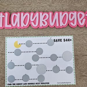 Puede incluir: Un letrero rosa y blanco que dice "catladybudgets" está encima de una tarjeta blanca con círculos grises y el texto "SAVE 44€+". La tarjeta también tiene el texto "FIND THE GHOST AND DOUBLE NEXT SCRATCH".