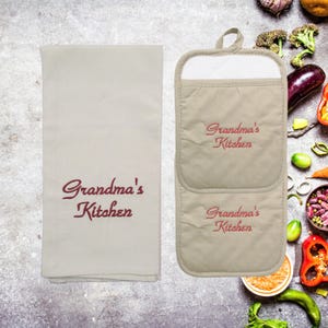 May include: A set of two beige kitchen pot holders with the text "Grandma's Kitchen" embroidered in red. A matching beige kitchen towel with the same text is also included.