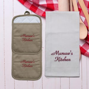May include: A set of two beige pot holders and a beige kitchen towel with the text "Mamaw's Kitchen" embroidered in red.