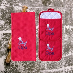May include: Red kitchen towel and pot holders with white quilted lining. Both items feature embroidered blue text that reads "Chef Opa" with a small chef hat graphic above the text.