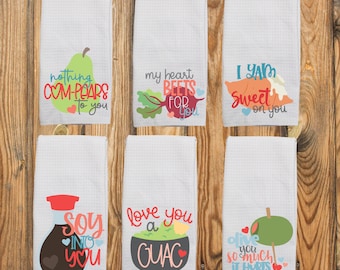 May include: Six white waffle-textured kitchen towels, each featuring a colorful food illustration and pun text: a pear with 'nothing COM-PEARS to you', a beet with 'my heart BEETS FOR you', a yam with 'I YAM sweet on you', soy sauce with 'SOY INTO YOU', guacamole with 'love you a GUAC', and an olive with 'olive you so much it hurts'.