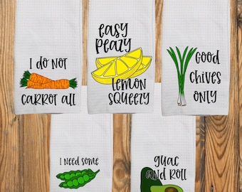 May include: Five white waffle-weave kitchen towels featuring food illustrations and puns. The towels display carrots with 'I do not carrot all', lemon slices with 'easy peasy lemon squeezy', chives with 'good chives only', peas with 'I need some peas and quiet', and an avocado with 'guac and roll'.