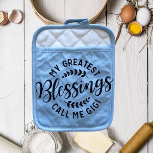 May include: Blue quilted oven glove with the text "My Greatest Blessings Call Me Gigi" in black lettering with a floral design.