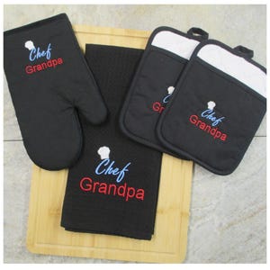 May include: A black kitchen set consisting of one oven mitt, two square pot holders, and one waffle-weave towel. Each item features an embroidered white chef hat icon above the blue text "Chef" and the red text "Grandpa" in a script font.