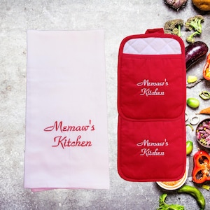 May include: Red and white kitchen pot holders with the text "Memaw's Kitchen" embroidered on them. The pot holders are on a white kitchen towel with the same text embroidered on it.