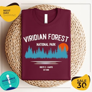 a burgundy t-shirt with a graphic design of a forest scene, along with text indicating it is a t-shirt for the Viridian Forest National Park.