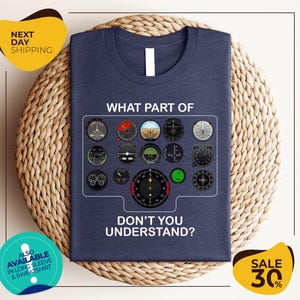 a blue t-shirt with a graphic design of various flight instruments and a question asking "Don't you understand?". The t-shirt is displayed on a woven placemat, and there are two yellow circular signs in the image.