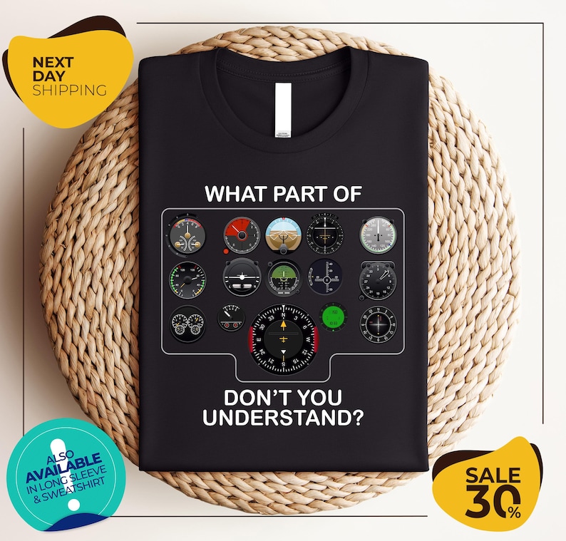 a black t-shirt with a graphic design of various flight instruments and a question asking "What part of don't you understand?". The t-shirt is displayed on a woven placemat, and there are two yellow circular banners with text around the image.