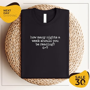 a black t-shirt with a humorous text printed on it, placed on a woven placemat.