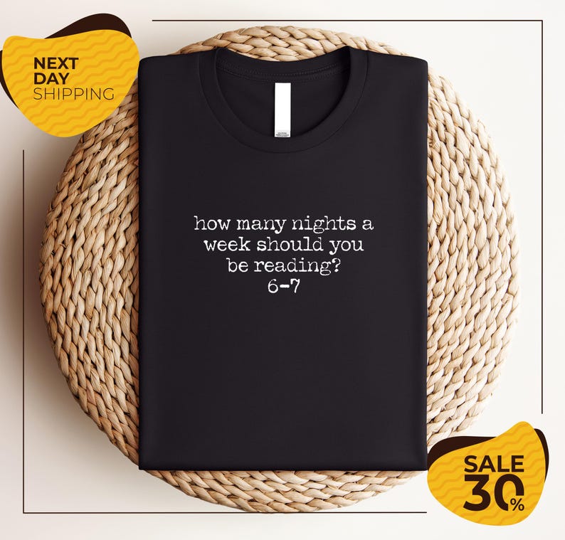 a black t-shirt with a humorous text printed on it, placed on a woven placemat.