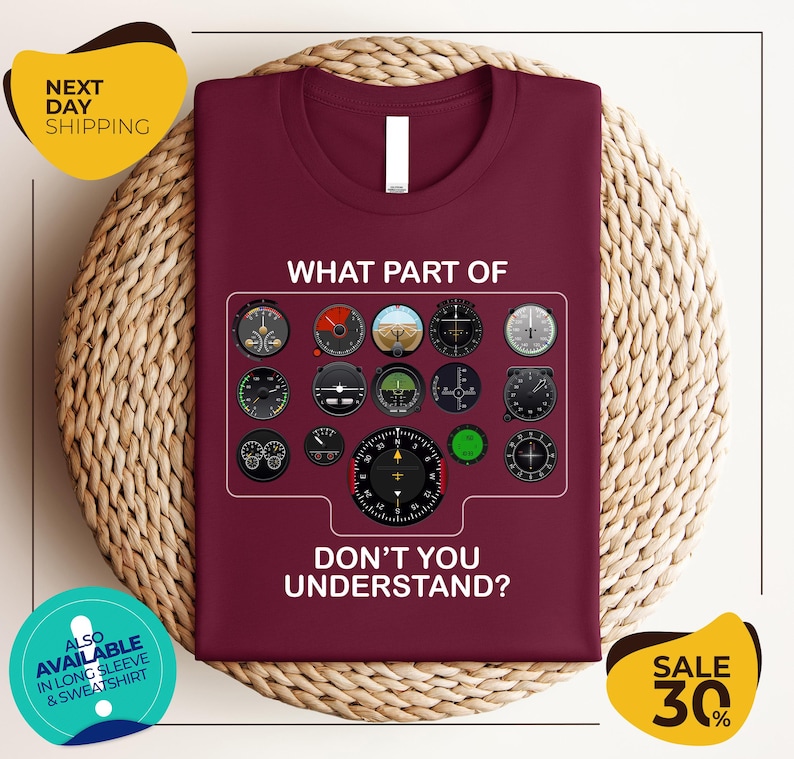 a maroon t-shirt with a graphic design of various flight instruments and a question asking "What part of don't you understand?". The t-shirt is displayed on a woven placemat, and there are two yellow circular banners with text around the image.