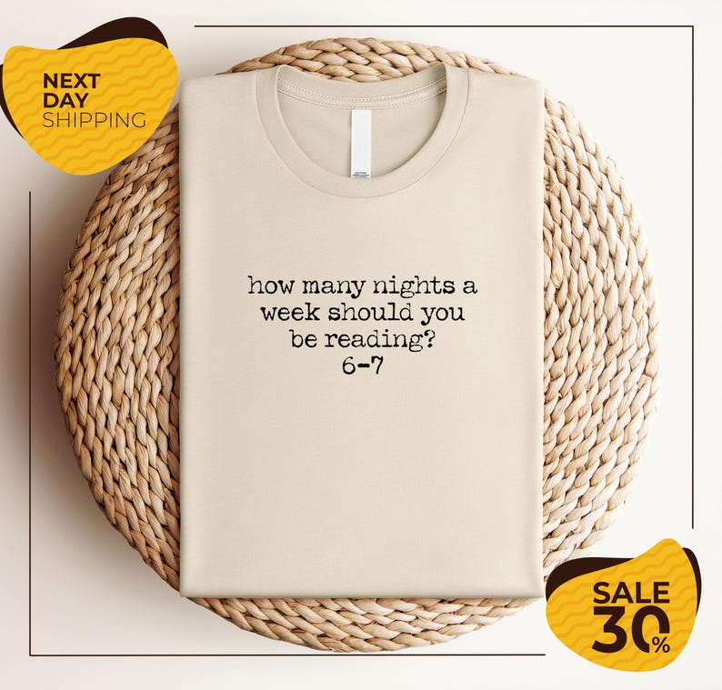A beige t-shirt with a humorous text printed on it, placed on a woven basket or mat.