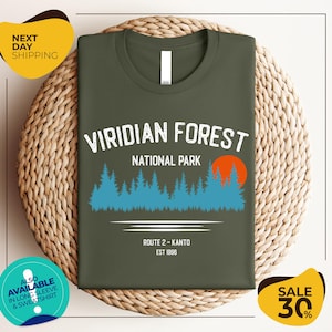 a green t-shirt with a graphic design of a forest and a route, along with text indicating it is from Viridian Forest National Park.