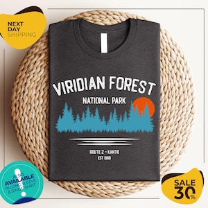 a gray t-shirt with a graphic design of a forest and a sunset, along with text indicating it is a t-shirt for the Viridian Forest National Park.