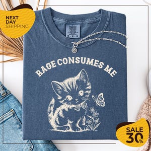a blue t-shirt with a white cat and flowers printed on it, along with a necklace and a yellow sign that reads "SALE 30%".
