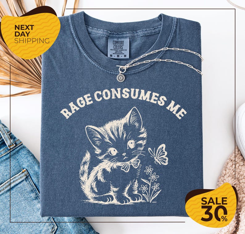 a blue t-shirt with a white cat and flowers printed on it, along with a necklace and a yellow sign that reads "SALE 30%".