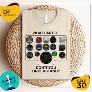 a t-shirt with a graphic design depicting various flight instruments and a question asking "What part of don't you understand?". The t-shirt is displayed on a woven placemat, and there are two yellow circular stickers with text around the image.