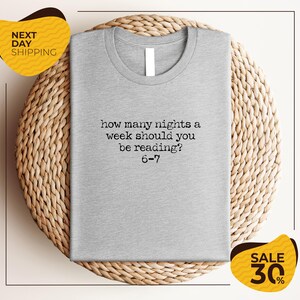 A gray t-shirt with a humorous text printed on it, placed on a woven placemat.