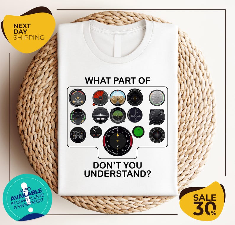 a white t-shirt with a graphic design depicting various flight instruments and the text "WHAT PART OF DON'T YOU UNDERSTAND?" The t-shirt is displayed on a woven placemat, and there are two yellow circular stickers with text on them.