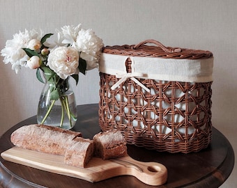 May include: A brown wicker basket with a white fabric lining and a handle, next to a wooden cutting board with sliced bread. A clear glass vase holds white peonies, creating a rustic, homey scene.