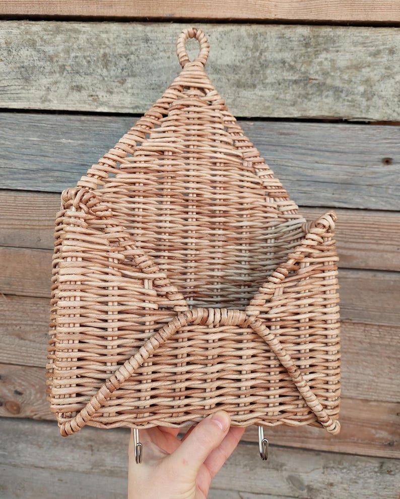 May include: A woven wicker wall organiser with two hooks. The organiser is shaped like an envelope and has a light brown colour.