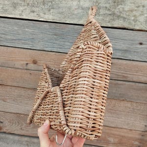 May include: A woven wicker wall hanging basket with a metal hook. The basket is light brown and has a natural woven texture.