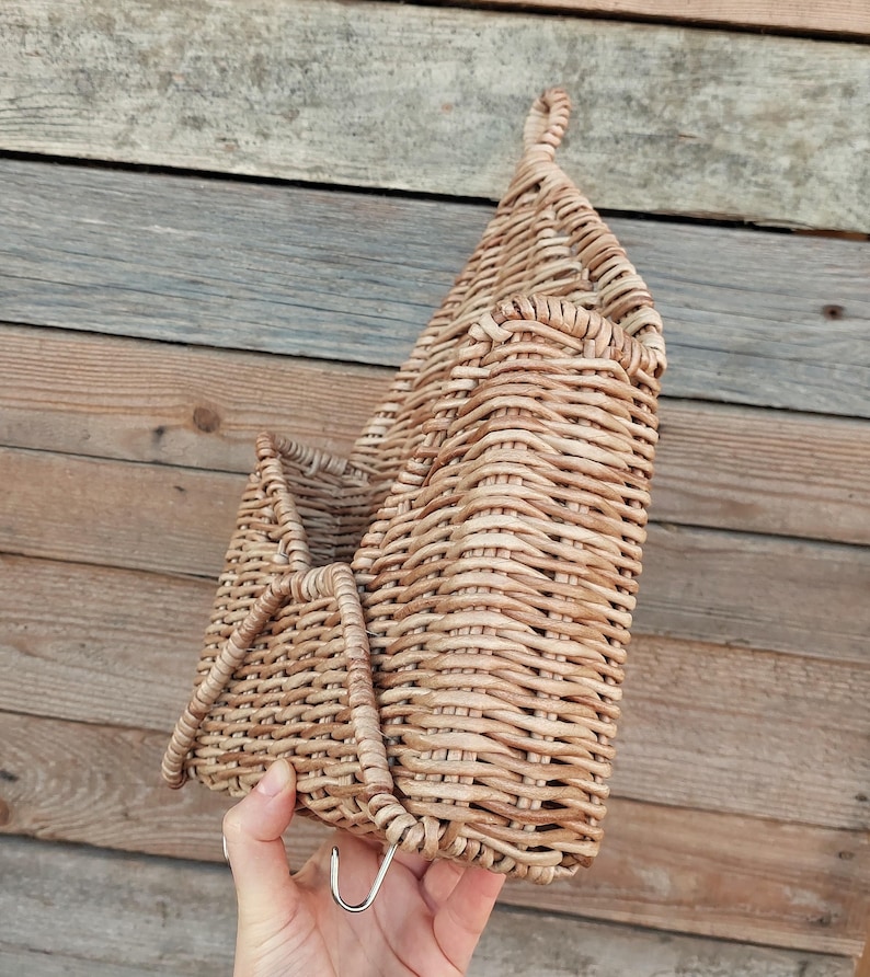 May include: A woven wicker wall hanging basket with a metal hook. The basket is light brown and has a natural woven texture.