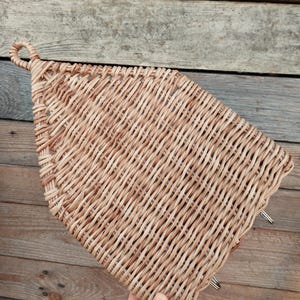 May include: A woven wicker basket with a handle in the shape of a house. The basket is light brown and has a natural, rustic look.