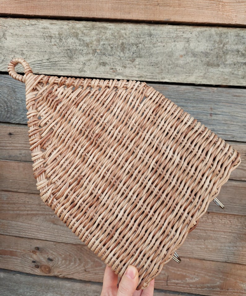 May include: A woven wicker basket with a handle in the shape of a house. The basket is light brown and has a natural, rustic look.