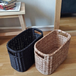 May include: Two woven storage baskets, one black and one brown, with oval shapes and two handles on each side.