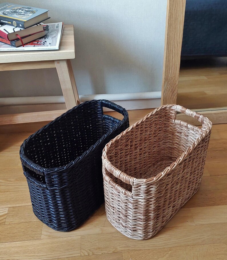 May include: Two woven storage baskets, one black and one brown, with oval shapes and two handles on each side.