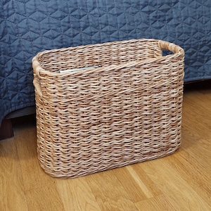 May include: A woven wicker basket with two handles. The basket is oval shaped and has a natural brown colour.